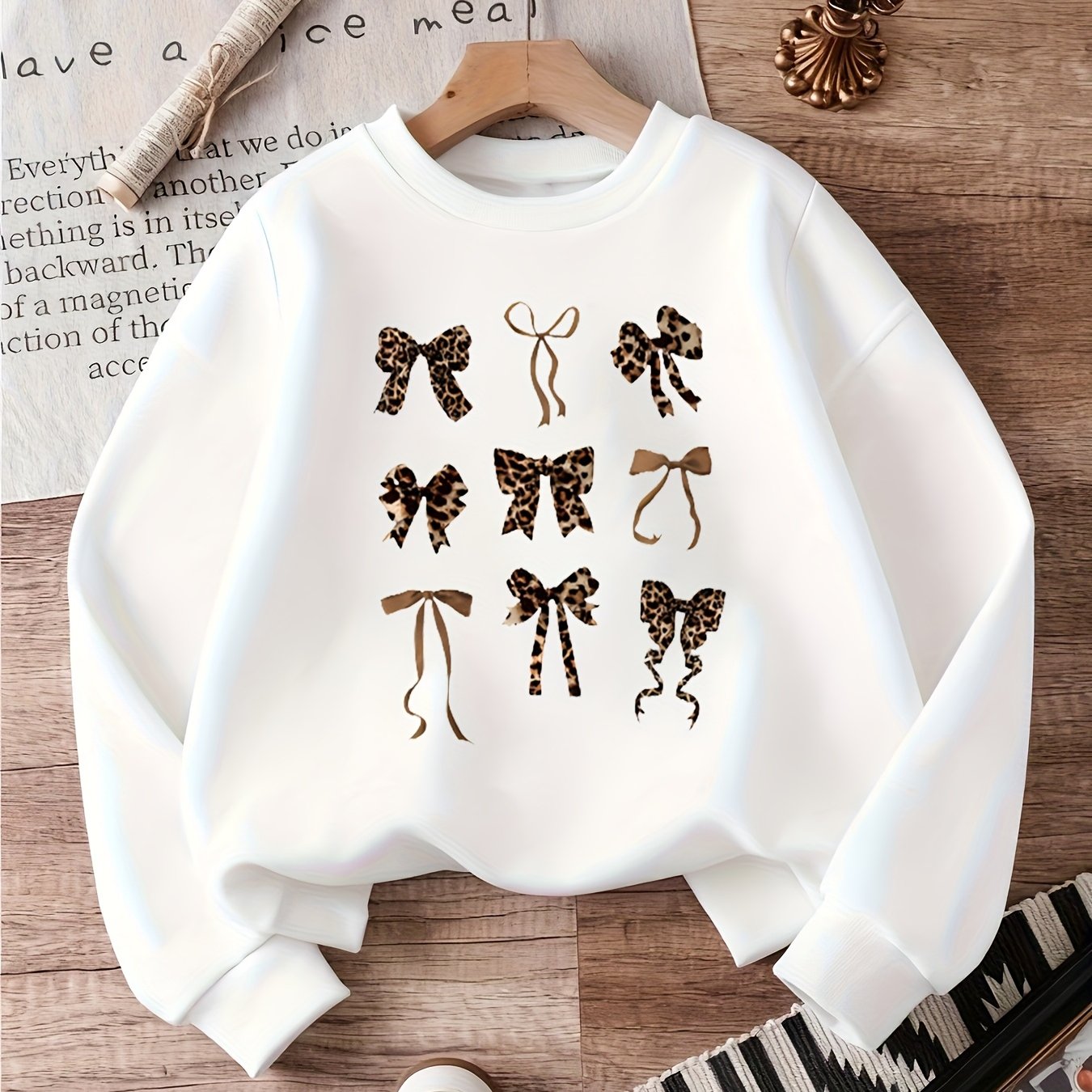 White women's crewneck sweatshirt with a 3x3 grid of leopard-print and solid bow graphics