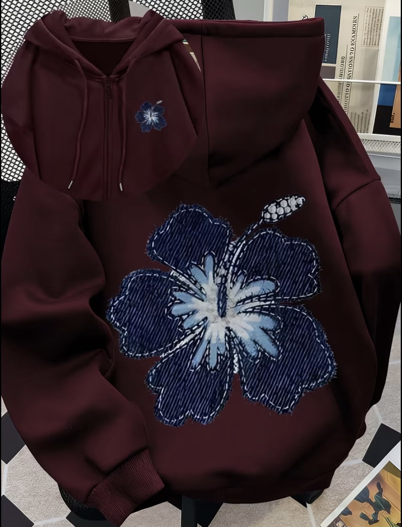 Maroon zip-up hoodie with a large textured blue floral graphic on the back and a matching small flower on the chest.